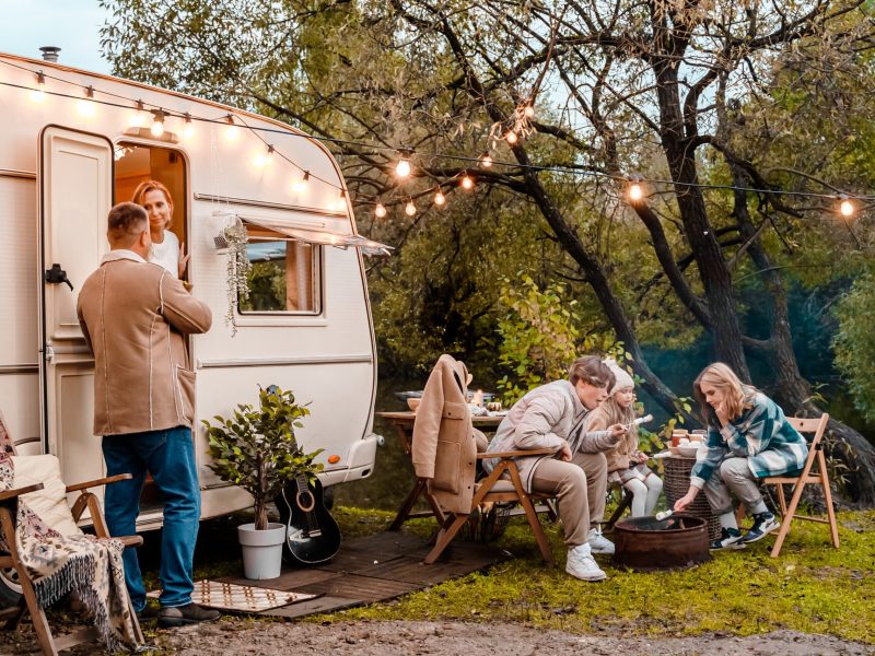 Family trailer travel. Children,brother sister,mom dad fry marshmallows on fire.Picnic in nature.Holiday barbecue BBQ food.Vacation weekend dinner.Road lunch snack.Camper,house on wheels,table chairs